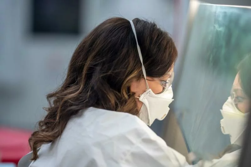 A virologist doing work in a lab with a mask and safety glasses on