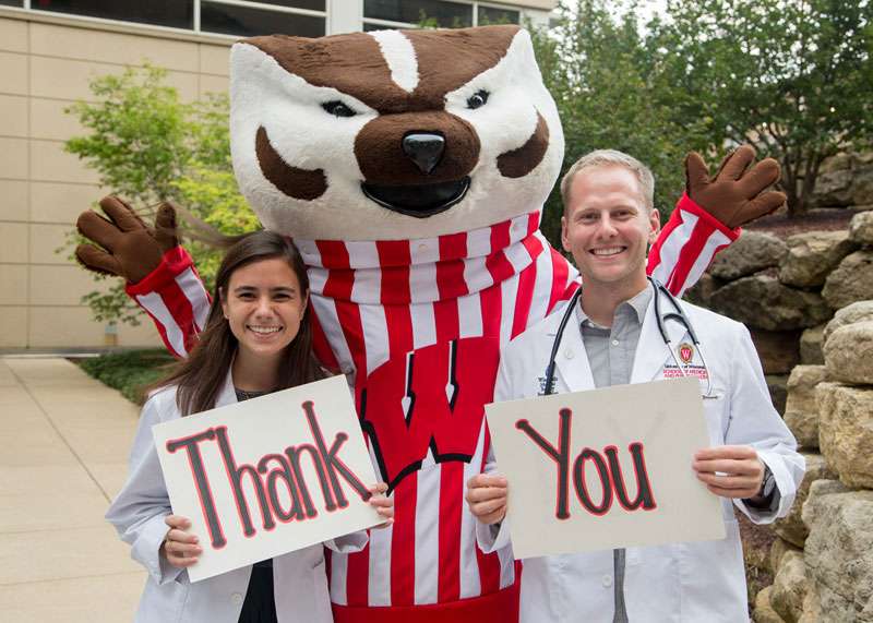 Two medical students holding signs, one that says 'Thank' and another that says 'You'